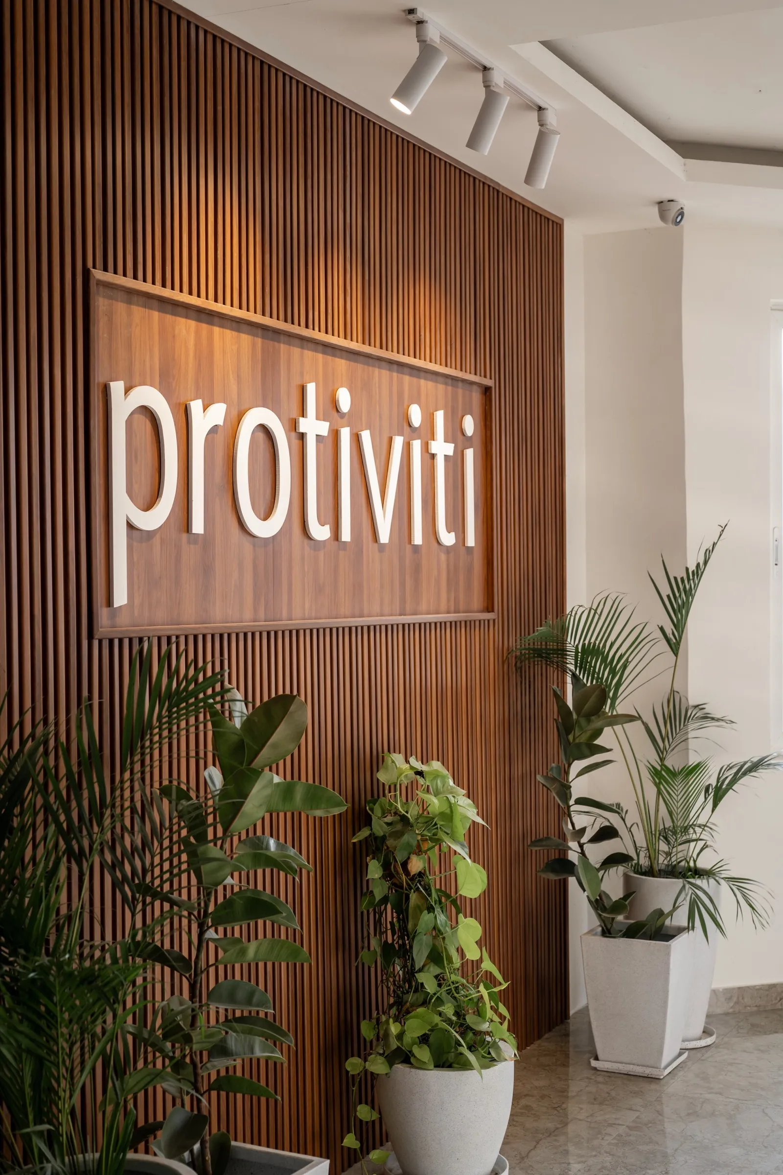 Protiviti logo on a vertical timber-slat feature wall with planters