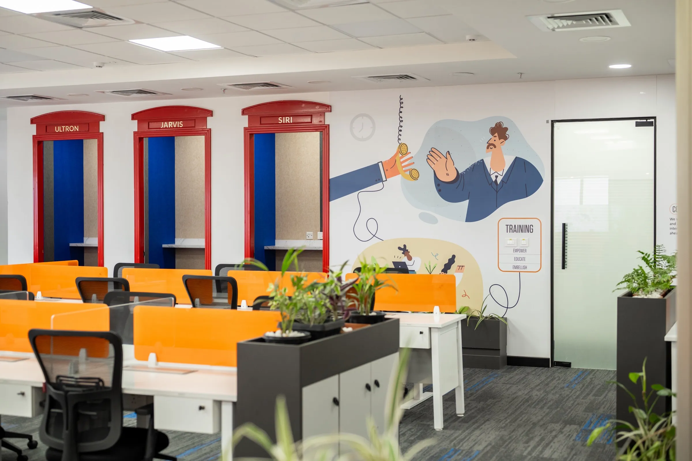 Red phone-booth style pods beside orange-screened workstations