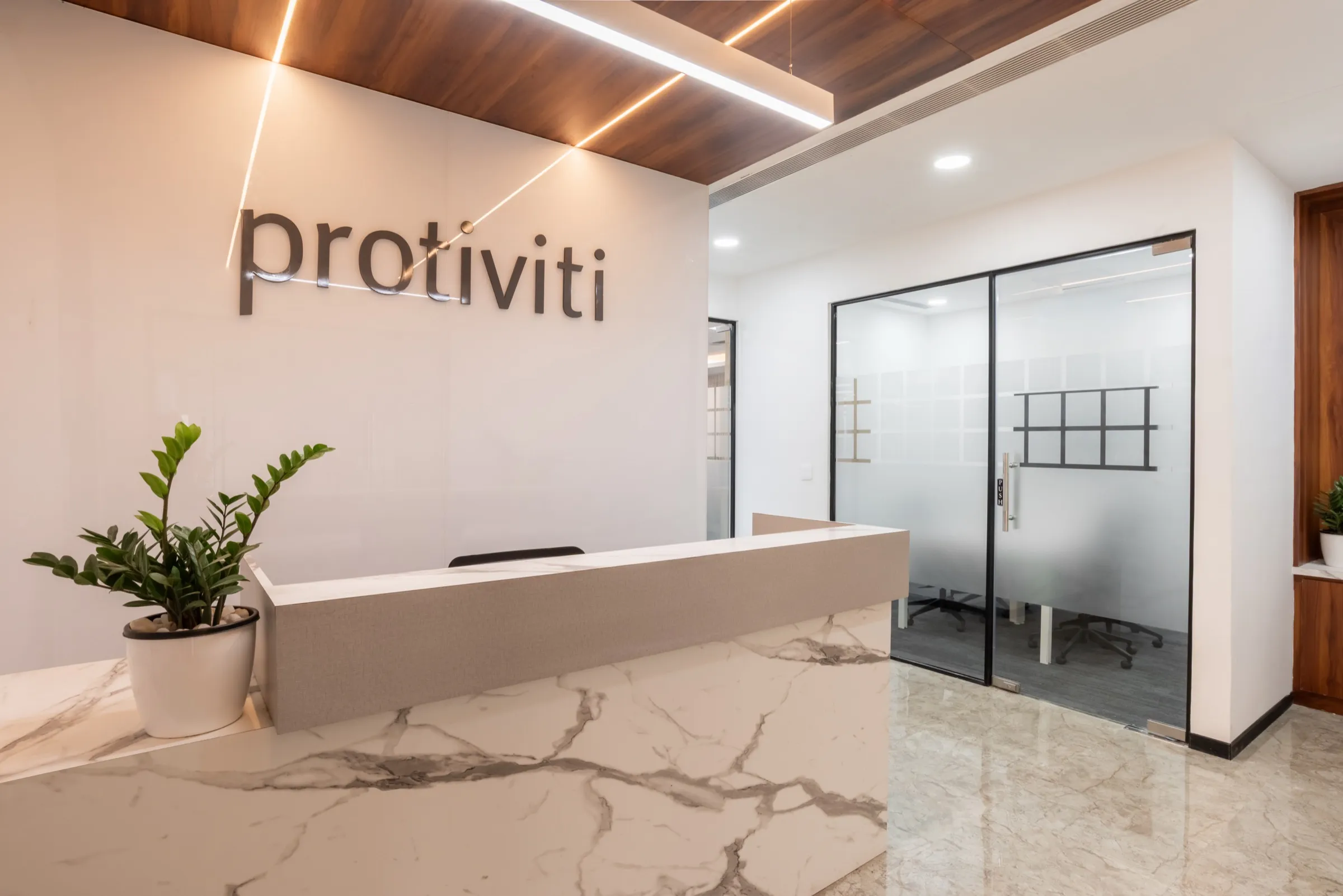 Protiviti reception with the brand logo, a white stone-finish desk and frosted glass partitions